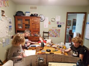 View from the head of the table. Meagan is sitting as the Dungeon Master running the game. The kids are around the table playing and Grandma is on the phone. 