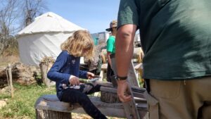 Arya using a draw knife to trim some wood. 